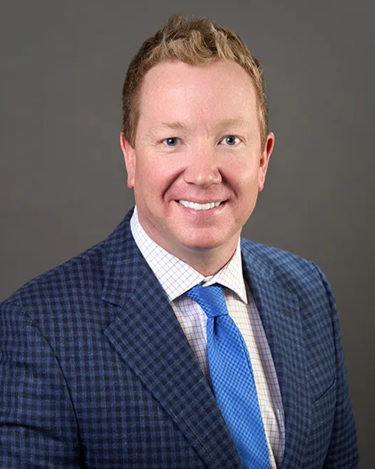 Dr. Adam Lukens pictured with a white collared shirt, royal blue tie, and navy plaid blazer